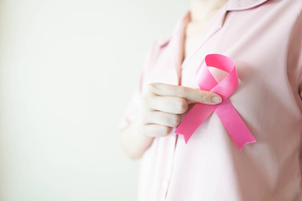 A close-up shot of a woman holding a pink ribbon up to her chest