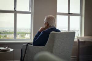 An elderly man sitting in a chair, looking out the window