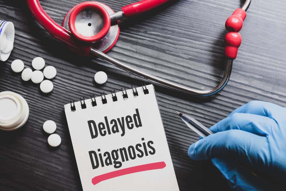 A stethoscope and white pills on a table next to a notepad that has “Delayed Diagnosis” written on it
