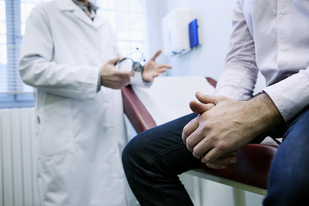 A cropped shot of a doctor talking to a man sitting on an exam table