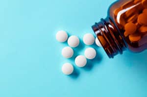 White pills spilling out of a bottle on a blue backdrop