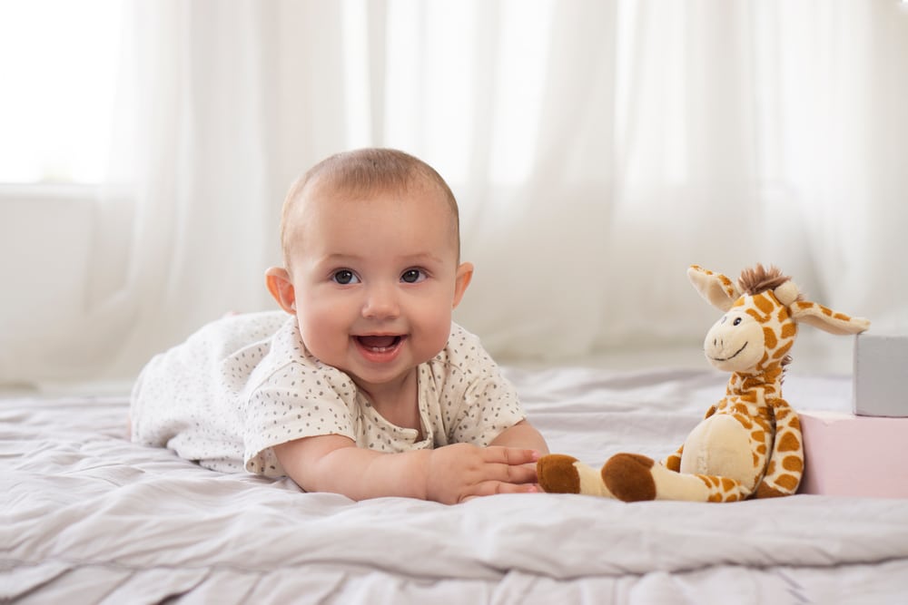 A baby lying on their stomach next to a stuffed giraffe