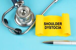A stethoscope and pen on a table with a piece of paper that says "Shoulder Dystocia"
