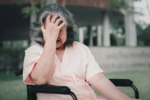 An elderly women with dementia sitting in a wheelchair with her head in her hand