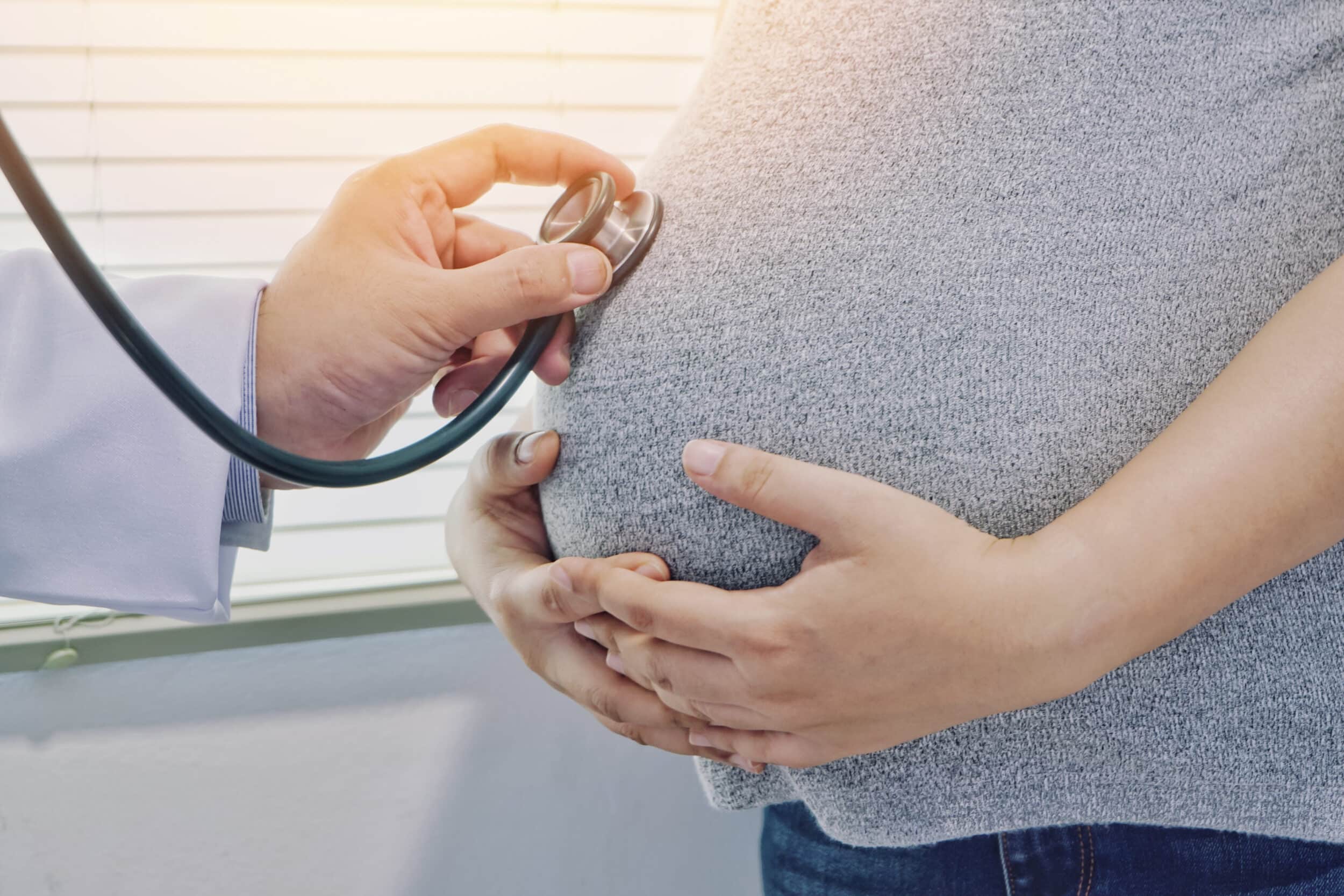 A doctor holding a stethoscope to a pregnant woman's stomach
