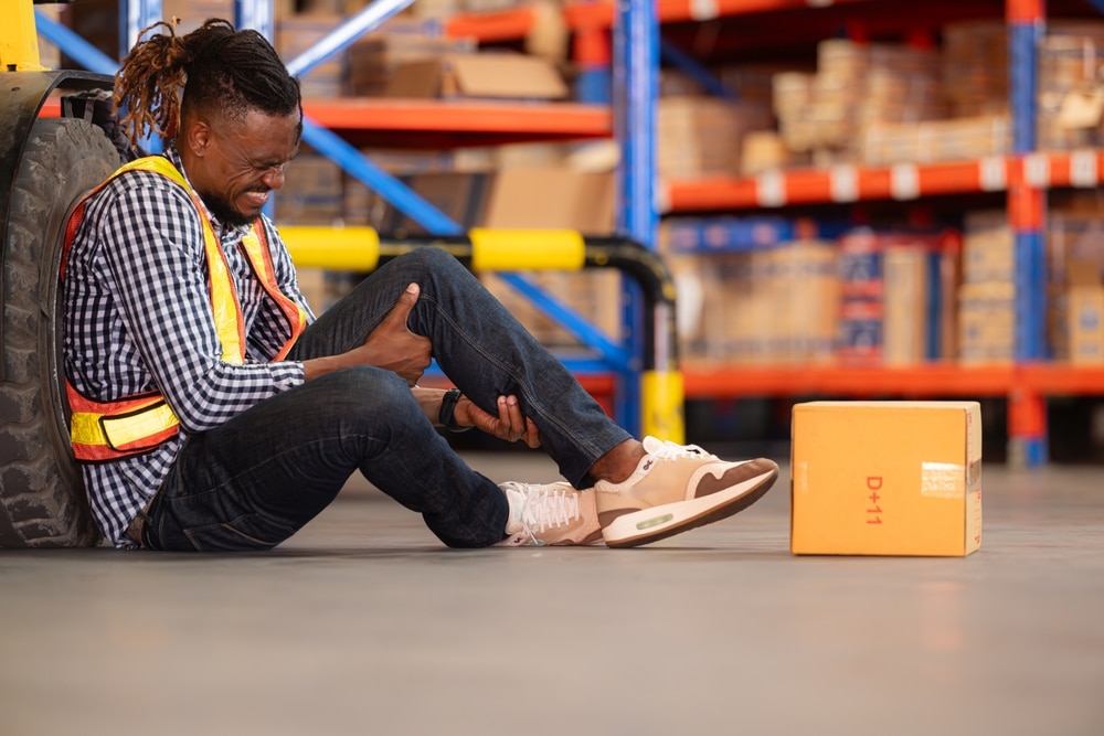 A temporary worker sitting on the ground holding his knee after a workplace accident