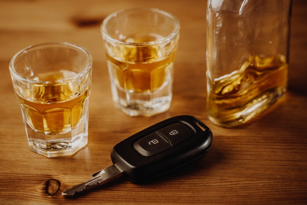A car key next to two shots glasses and a bottle of alcohol